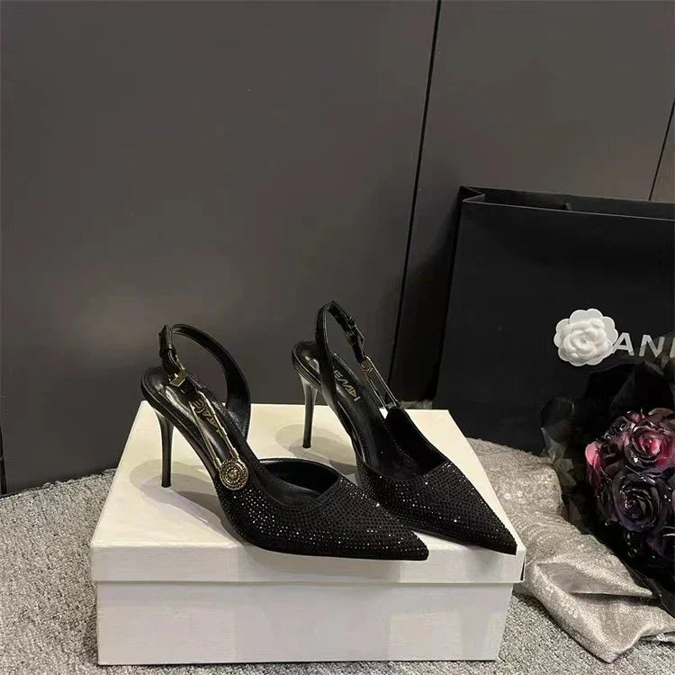Elegant black high-heeled slingback shoes with sparkling details displayed on a white box, luxury shopping bag nearby