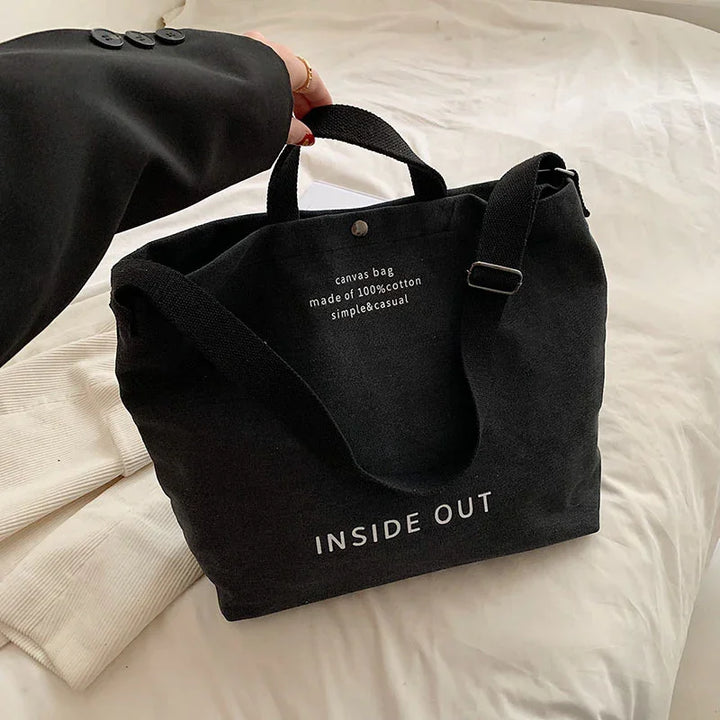 Black canvas tote bag with text inside out and made of 100% cotton, held by hand on white fabric