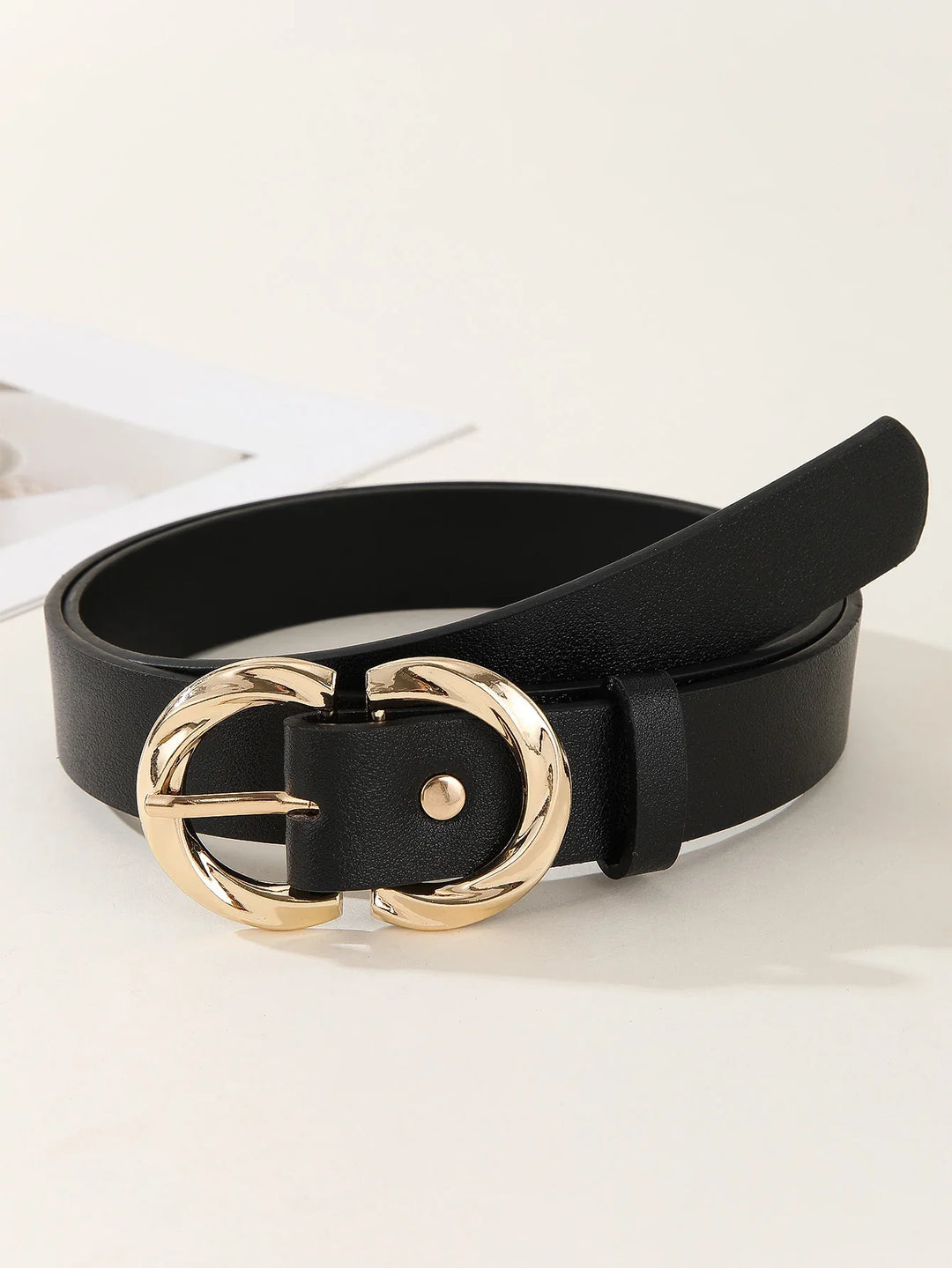 Black leather belt with twisted gold round buckle on white surface