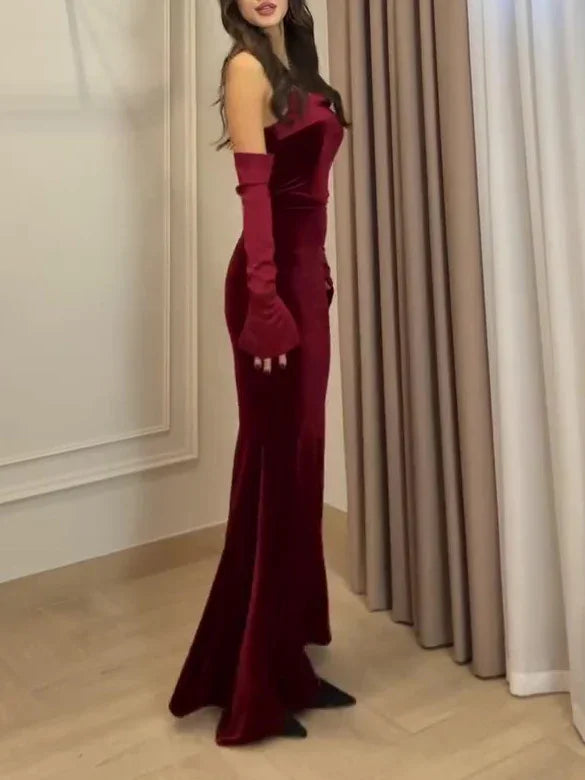 Woman wearing a fitted burgundy velvet evening gown with matching long gloves in a minimalist room