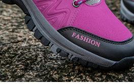 Close-up of vibrant pink hiking boot with black sole on rough outdoor terrain