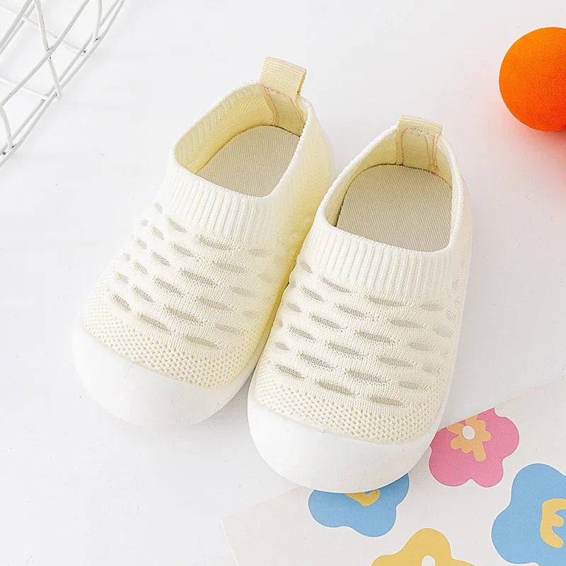 pair of cream-colored baby knit sneakers with textured uppers and white soles on white surface