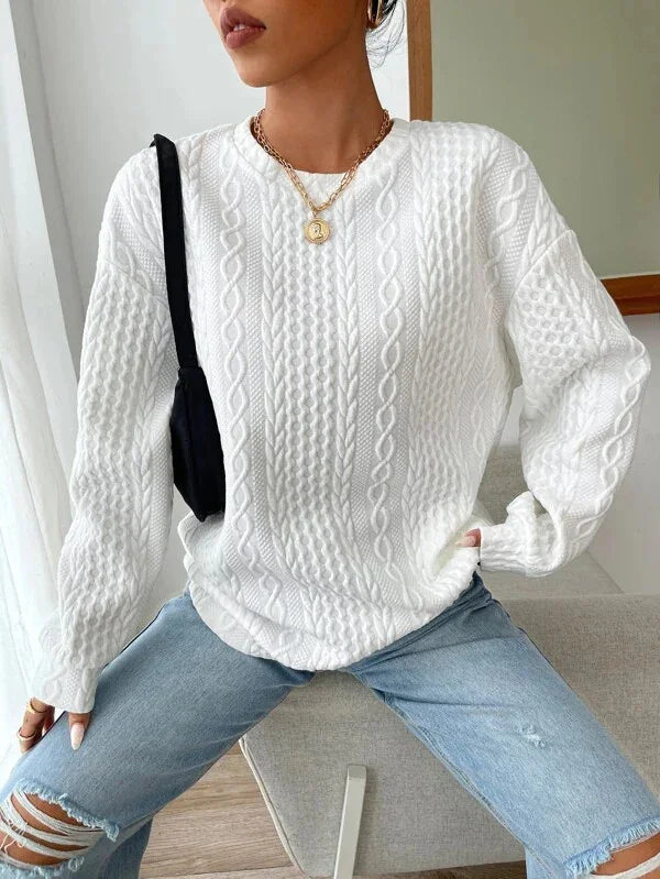 Woman wearing white cable knit sweater and ripped blue jeans with gold pendant necklace and black shoulder bag