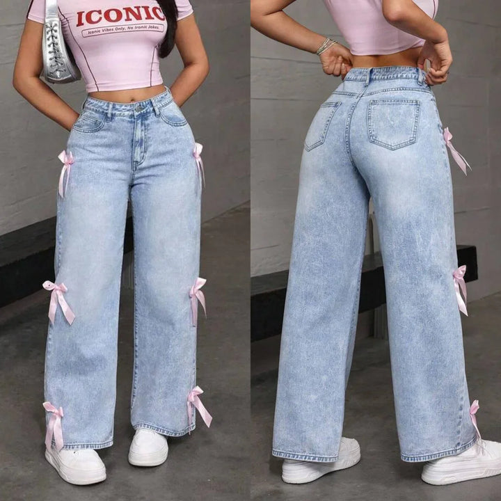 Woman wearing light blue wide-leg jeans with pink ribbon bows and a pink crop top with ICONIC text