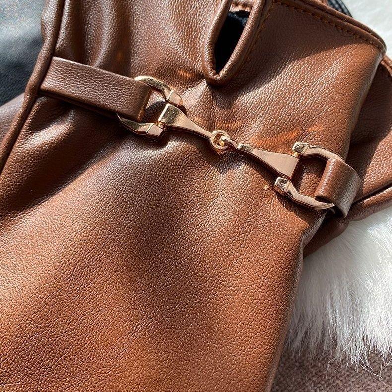 Close-up of brown leather glove with gold metal bit detail on a soft white fur surface