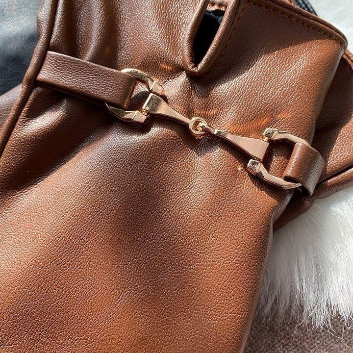 Close-up of brown leather glove with gold metal bit detail on a soft white fur surface