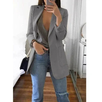Woman wearing gray blazer, deep V-neck top, ripped blue jeans, taking mirror selfie indoors