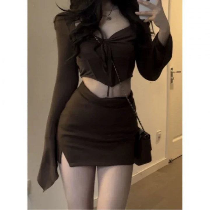 woman wearing black long-sleeve crop top and mini skirt with side slit, holding a black handbag indoors