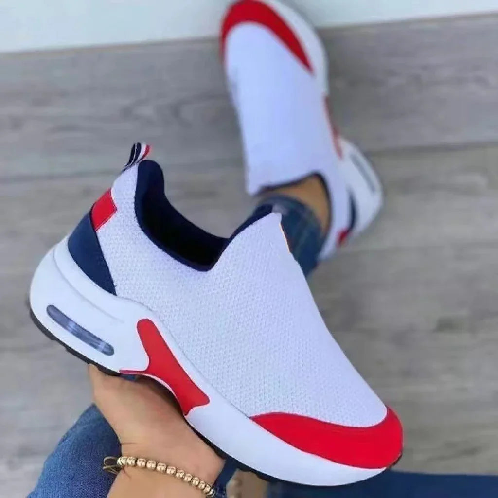 White slip-on sneakers with red and navy accents on a wooden floor background