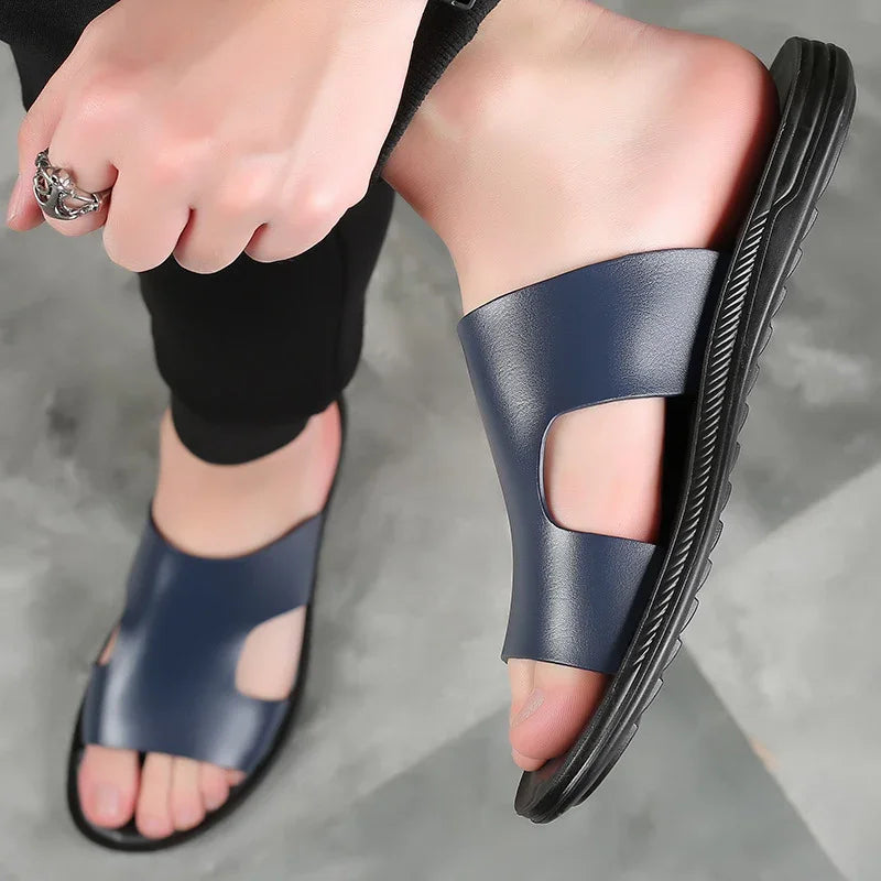 Close-up of feet wearing navy blue leather open-toe slide sandals with black soles on gray floor