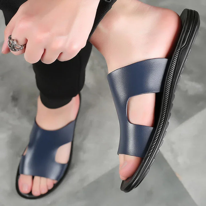 Close-up of feet wearing navy blue leather open-toe slide sandals with black soles on gray floor