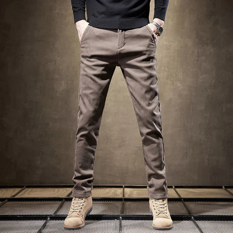 Man wearing slim fit brown casual pants with beige suede boots and black sweater on industrial floor