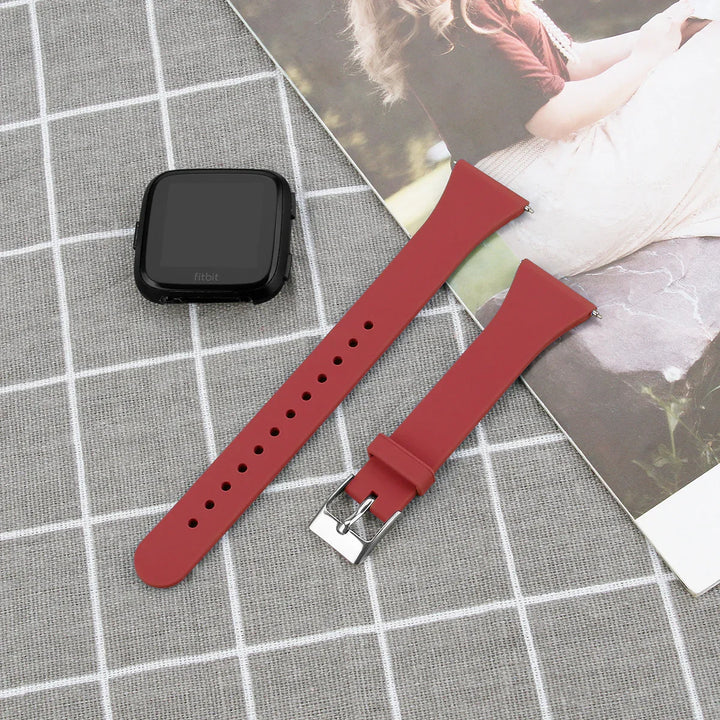 Disassembled black Fitbit smartwatch with detached red silicone watch bands on gray grid fabric