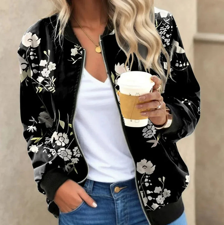 Woman wearing black floral bomber jacket, white tee, blue jeans holding coffee cup