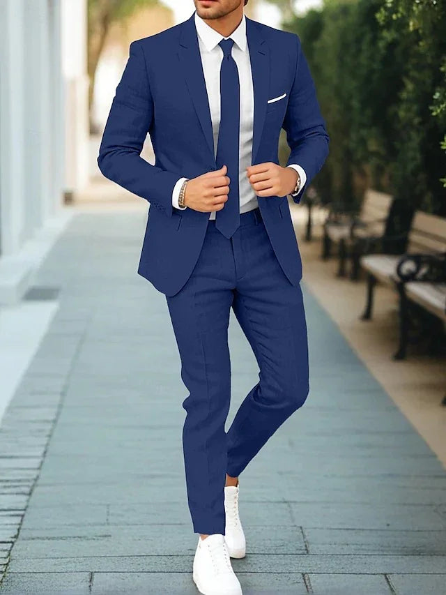 Man wearing a fitted blue suit with white shirt, blue tie, and white sneakers walking outdoors
