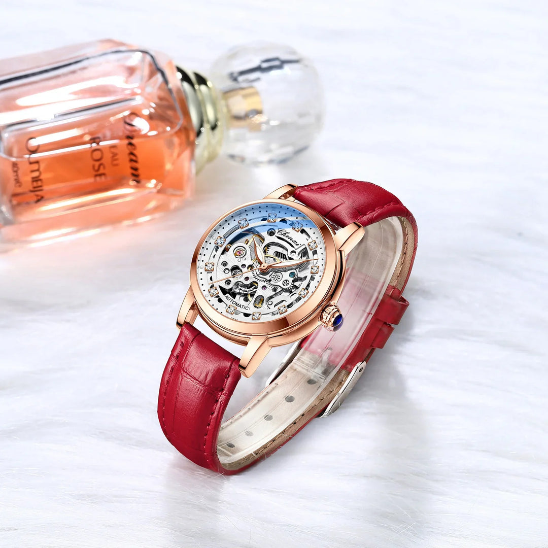 Rose gold automatic wristwatch with red leather strap and skeleton dial on white surface