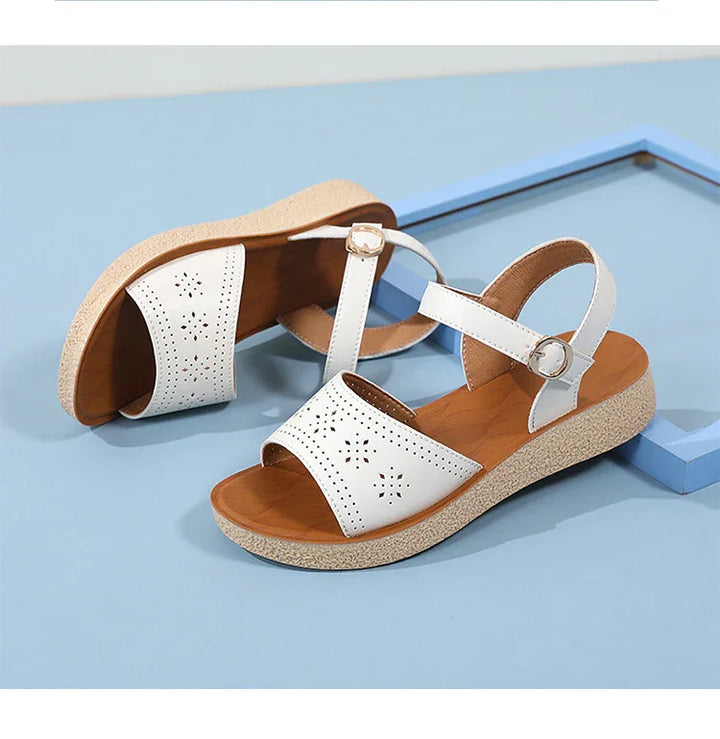 White leather women's sandals with perforated floral design and adjustable ankle straps on beige textured soles