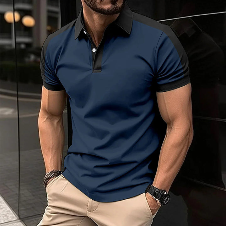 Muscular man wearing navy blue and black short sleeve polo shirt with beige pants, standing outdoors