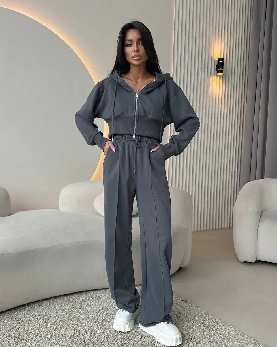 Woman in dark gray cropped hoodie and wide-leg pants with white sneakers in modern living room