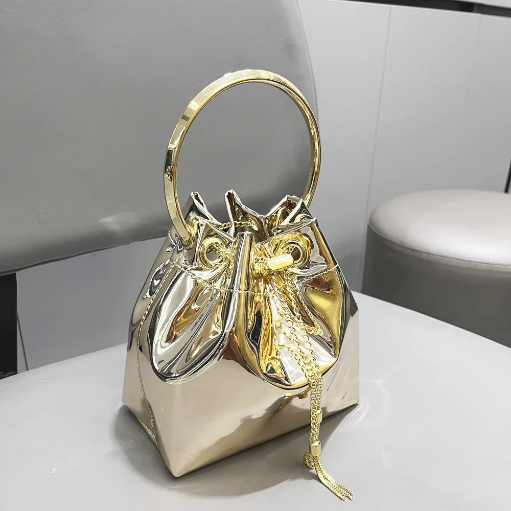 Shiny metallic gold handbag with circular top handle and drawstring closure on gray chair