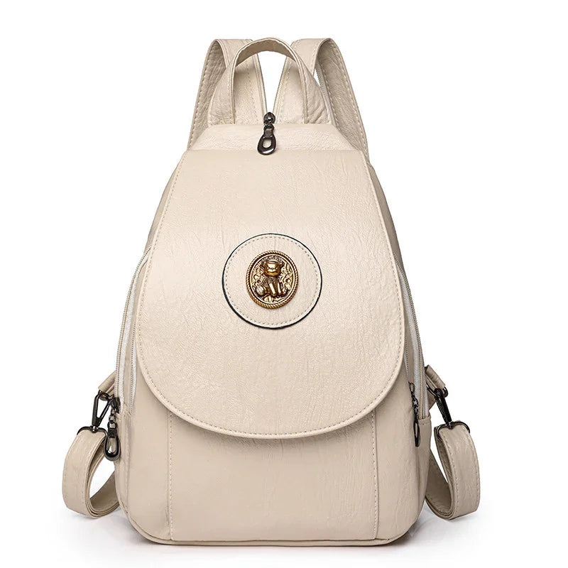 Cream leather backpack with front flap and gold monkey emblem, adjustable straps
