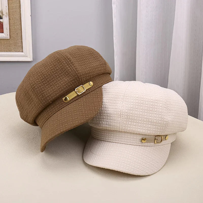 Brown and cream textured fabric newsboy caps with gold buckle accent on beige surface
