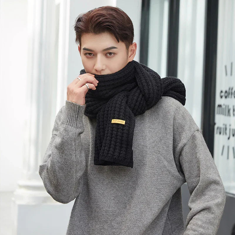 Young man wearing a black knitted scarf and gray sweater posing outdoors in urban setting
