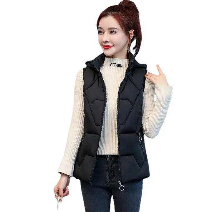 Woman wearing black padded sleeveless vest over cream ribbed turtleneck sweater and dark jeans