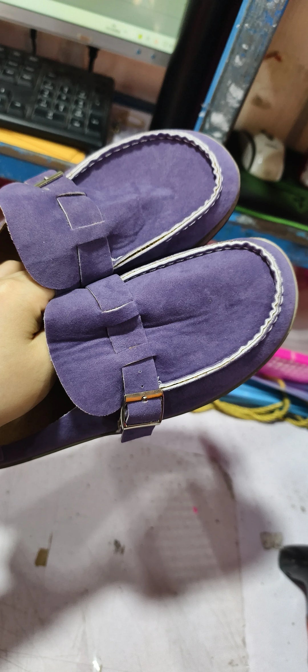 Pair of purple suede loafers with white stitching and metal buckle held by hand