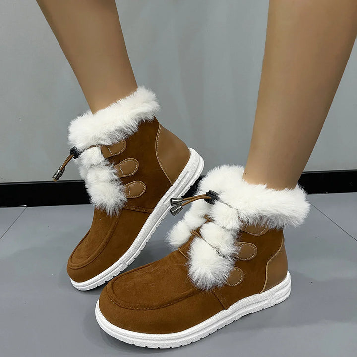 Brown winter boots with white fur trim and white soles worn on feet against gray floor