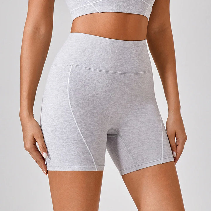 Woman wearing high-waisted light gray workout bike shorts with white stitching detail