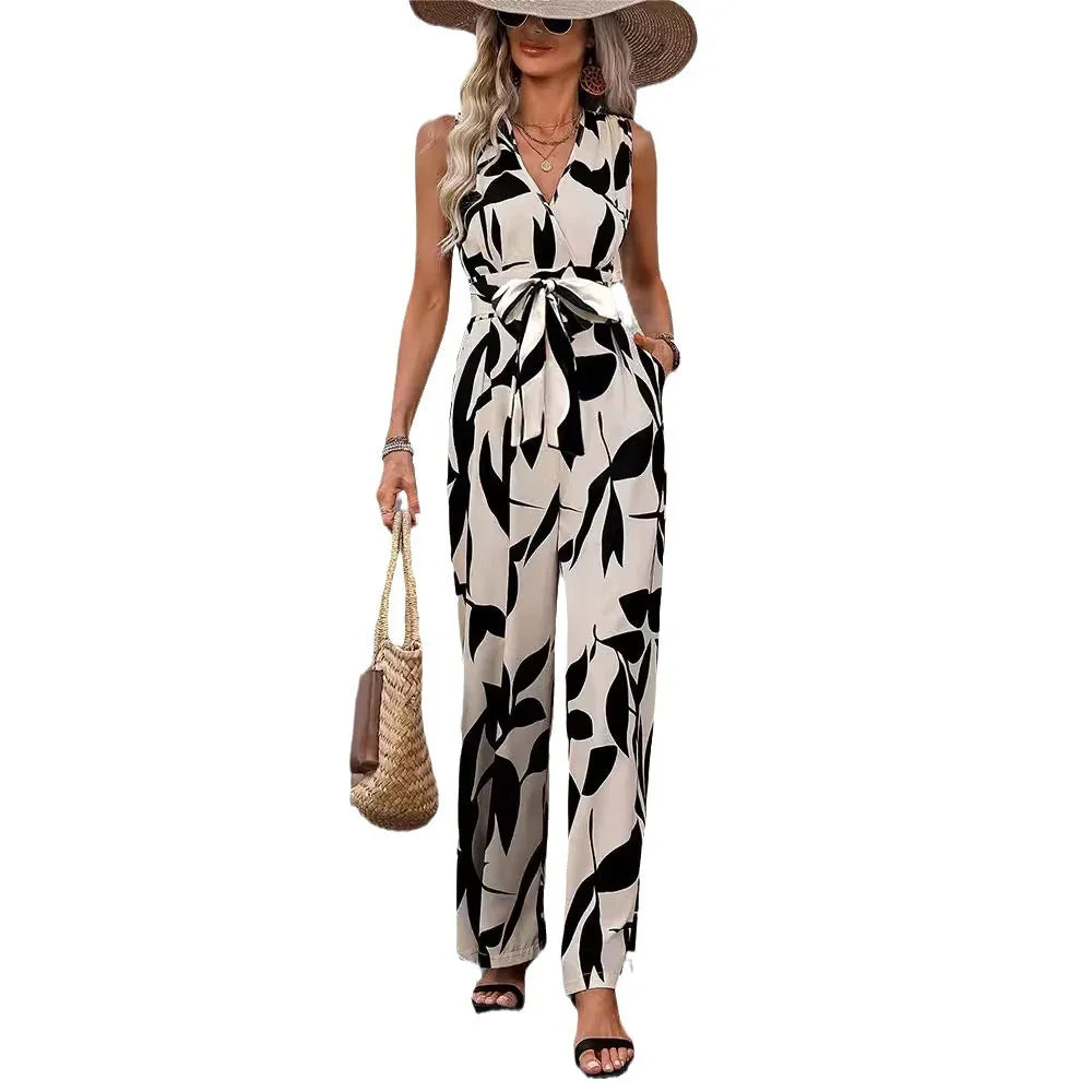 woman wearing sleeveless black and white leaf print jumpsuit with tie waist, sunglasses, straw hat, and handbag