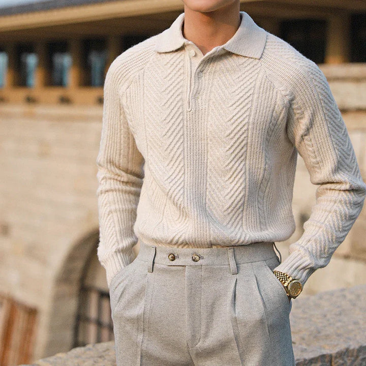 Close-up of man wearing cream cable knit sweater with collar and light gray pleated trousers outdoors