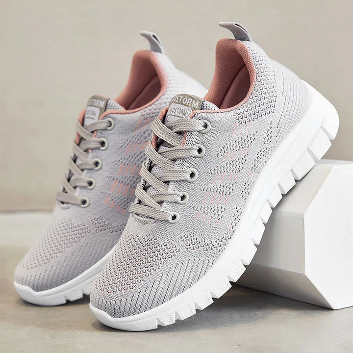 Light gray and pink knit athletic sneakers with white thick sole on gray and white background