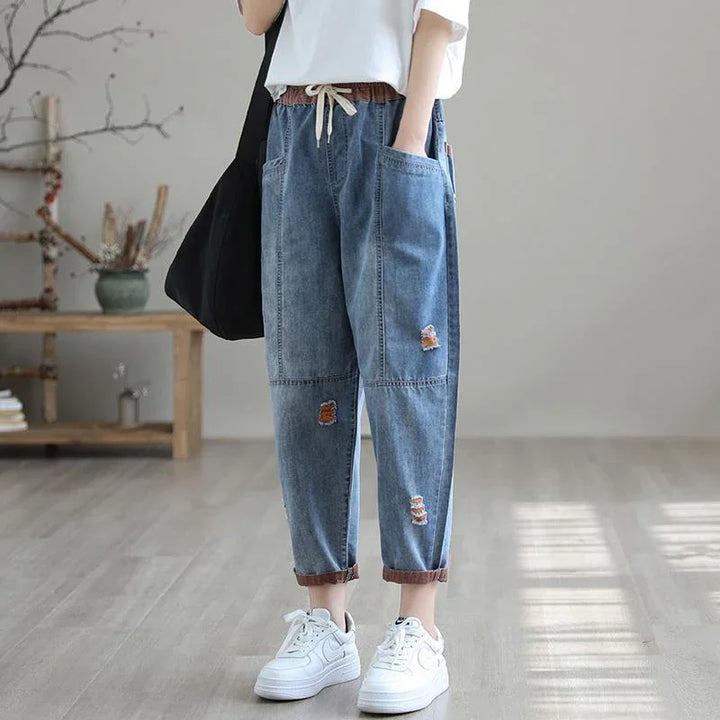 Casual loose-fit ripped denim pants with drawstring waist, worn with white sneakers indoors