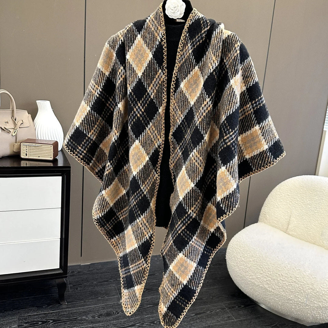 Black and beige plaid knit poncho draped on white hanger in modern room with white chair and dresser