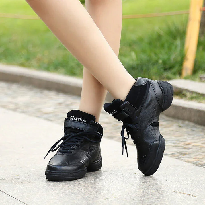 Person wearing black Sasha high-top dance sneakers on pavement with grass background