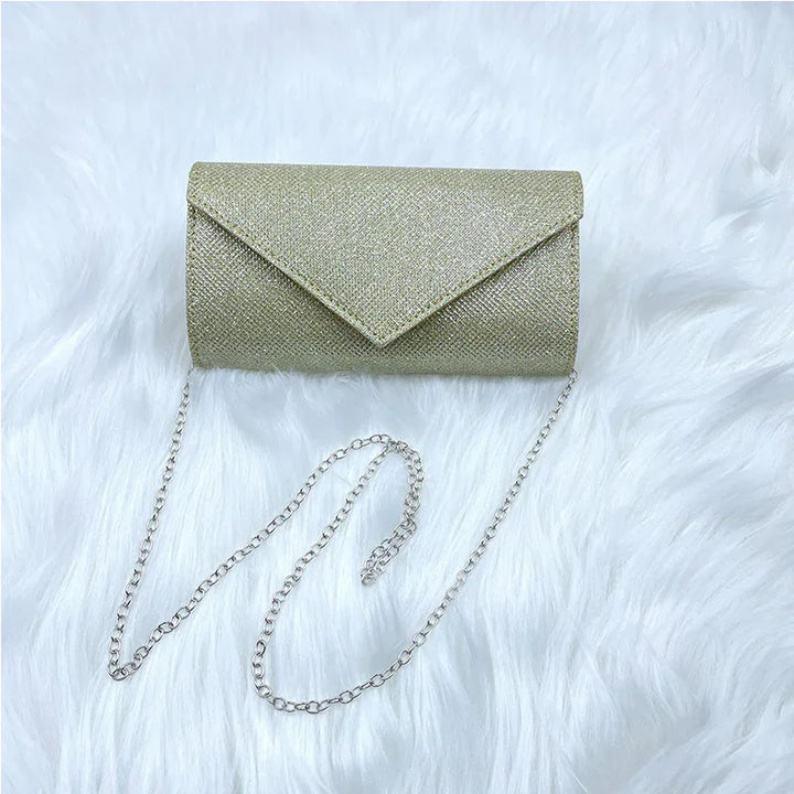 Gold glitter envelope clutch purse with silver chain on white faux fur background