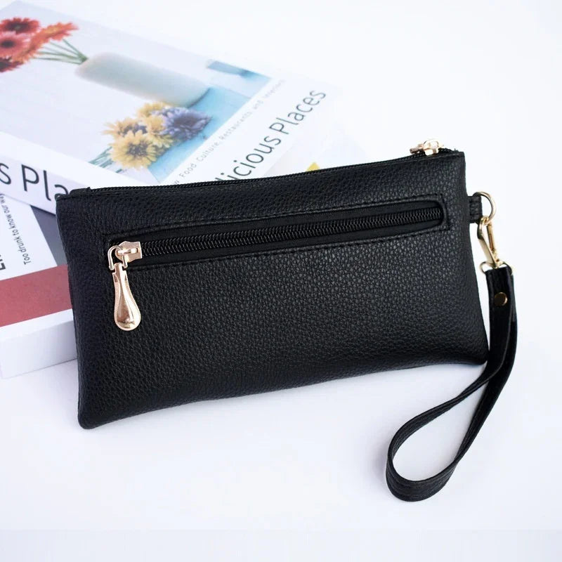 Black textured leather wristlet clutch with gold zipper and detachable strap, placed on books with floral covers