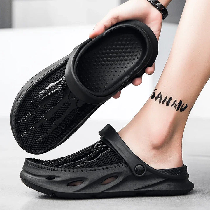 Black breathable mesh slip-on sandals with adjustable strap worn on foot with ankle tattoo