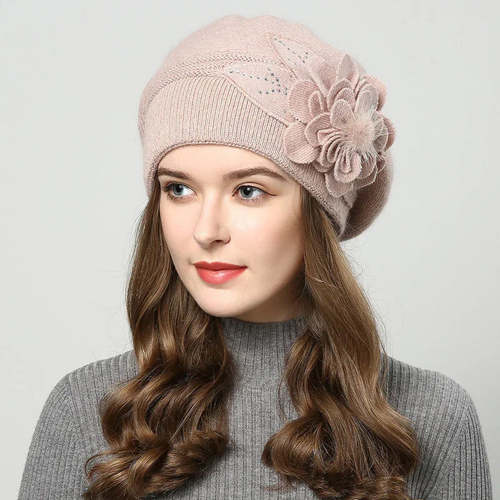 Woman wearing pink wool beret with flower detail and gray ribbed sweater