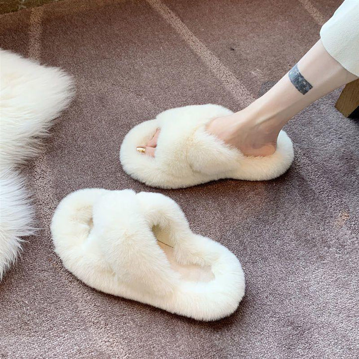 White fluffy faux fur open-toe slippers on carpet with a foot wearing one slipper