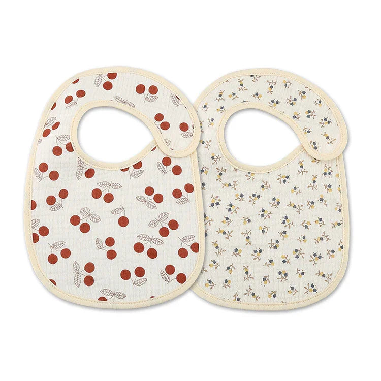 Set of two baby bibs with beige trim, one with red cherry print, the other with small floral design
