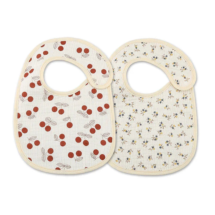 Set of two baby bibs with beige trim, one with red cherry print, the other with small floral design