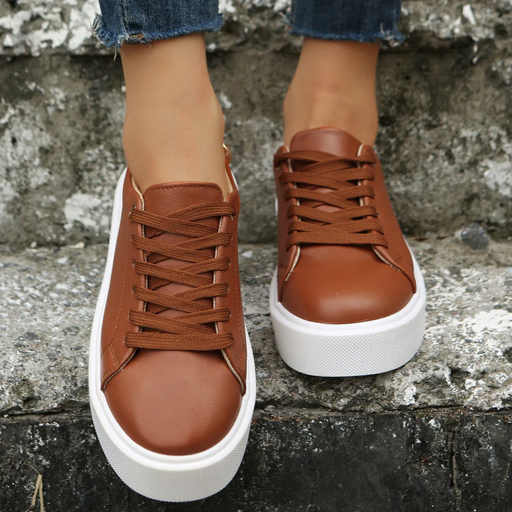 Close-up of brown leather sneakers with white thick soles worn with blue jeans on stone steps