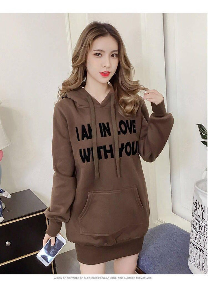 Young woman wearing brown hoodie dress with I AM IN LOVE WITH YOU text, holding smartphone indoors