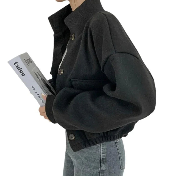 Woman wearing black cropped jacket with buttons holding a book, paired with blue jeans