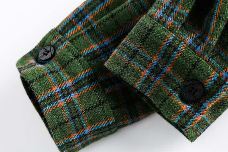 Close-up of green plaid wool fabric with blue and orange lines and black buttons on sleeves