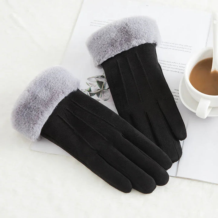 Black winter gloves with soft gray fur cuffs on white surface next to cup of coffee