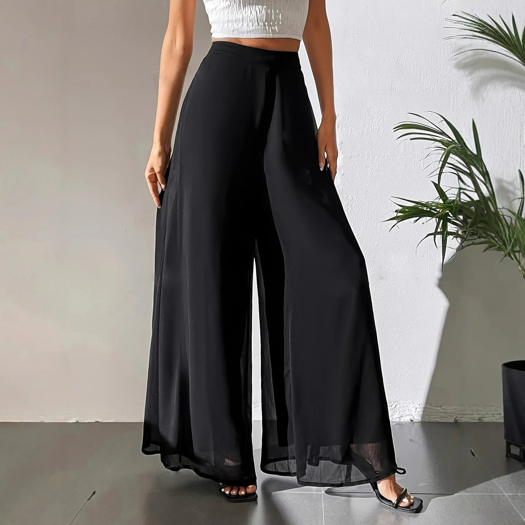 Woman wearing black wide-leg pants and a white cropped top in a minimalist indoor setting